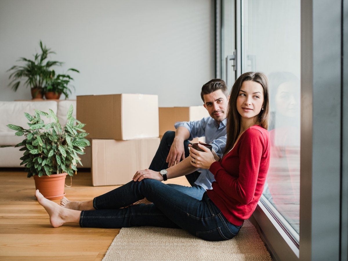 ¿Cuánto se tarda en vender un piso en Zaragoza? 1 Pareja sentada en el suelo junto a cajas de mudanza, pendiente de cuánto tarda vender su casa en Zaragoza