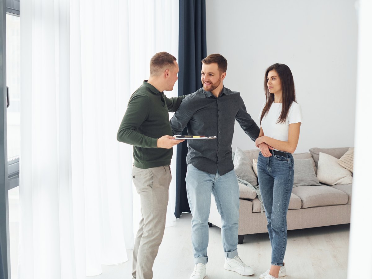 ¿Cuánto cobra una inmobiliaria por vender un piso en Zaragoza? Comisión, IVA y quién la paga 2 Agente inmobiliario con una pareja en el salón de un piso: cuánto cobra una inmobiliaria al comprador en Zaragoza