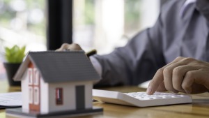 Casita de maqueta y calculadora sobre la mesa para calcular cuánto cobra una inmobiliaria por vender un piso en Zaragoza