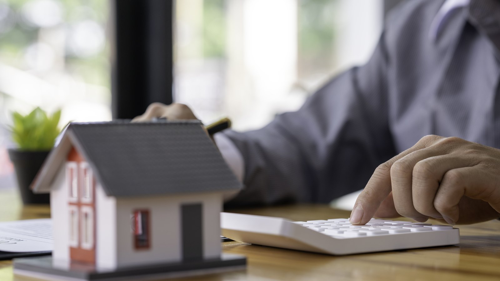 Casita de maqueta y calculadora sobre la mesa para calcular cuánto cobra una inmobiliaria por vender un piso en Zaragoza