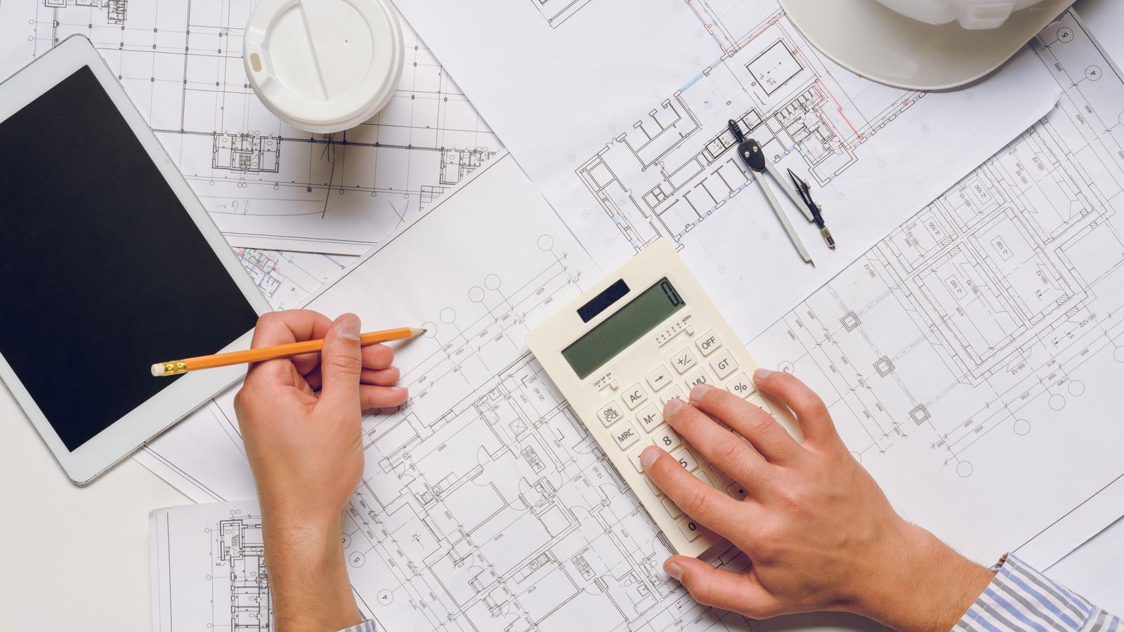 Técnico con planos, lápiz y calculadora calculando cuánto cuesta tasar un piso en Zaragoza