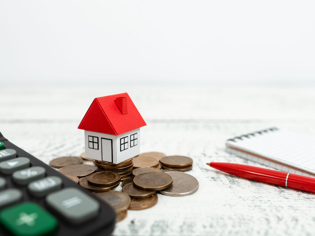 ¿Cuánto cobra una inmobiliaria por vender un piso en Huesca? Comisión, IVA y gastos 1 Casita sobre un montón de monedas junto a una calculadora: plusvalía municipal en Huesca