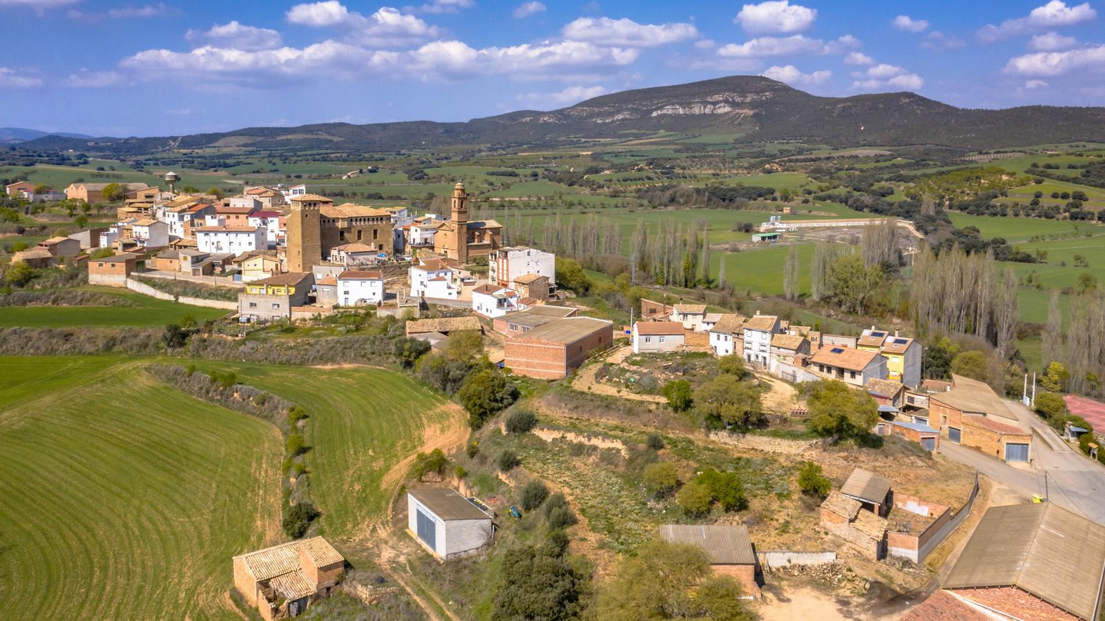 Pueblo de casas de ladrillo y piedra con su torre de iglesia, rodeado de campos de cereal y chopos